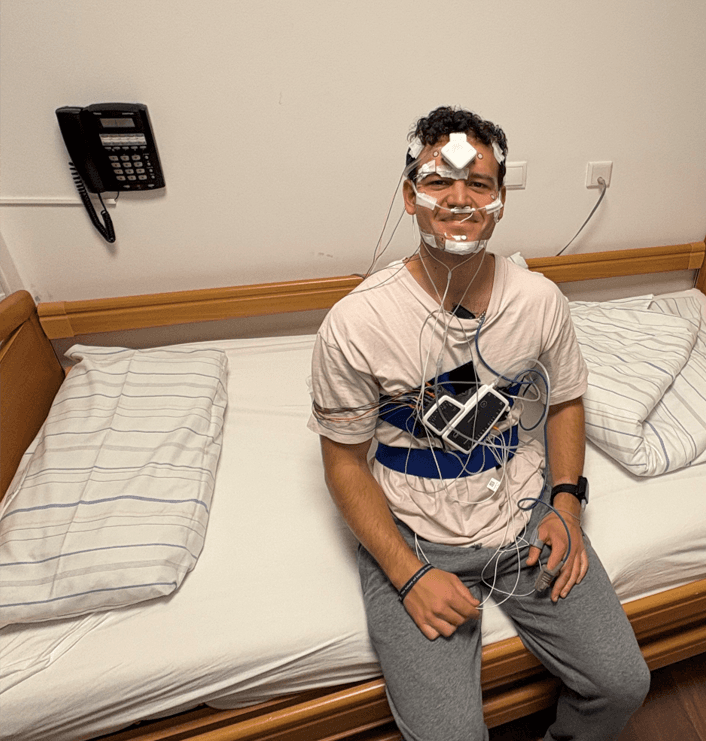 Marcello sitting on a bed wearing sensors for a sleep study.